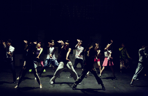 A troupe of thirteen dancer's perform a hip-hop dance routine on stage.